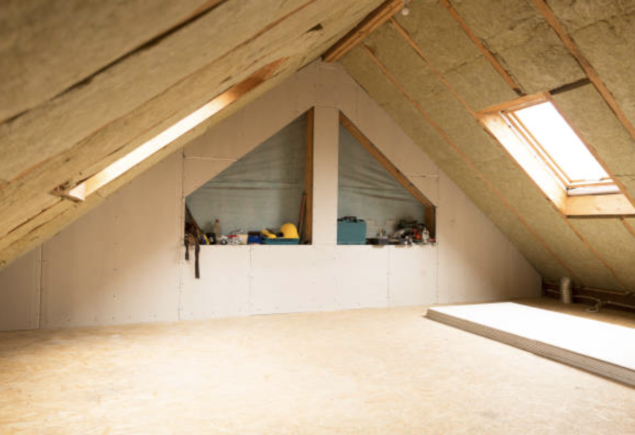 Combles en cours d’aménagement, avec isolation visible sous le toit, deux fenêtres de toit laissant entrer la lumière et des outils rangés dans un renfoncement du mur.