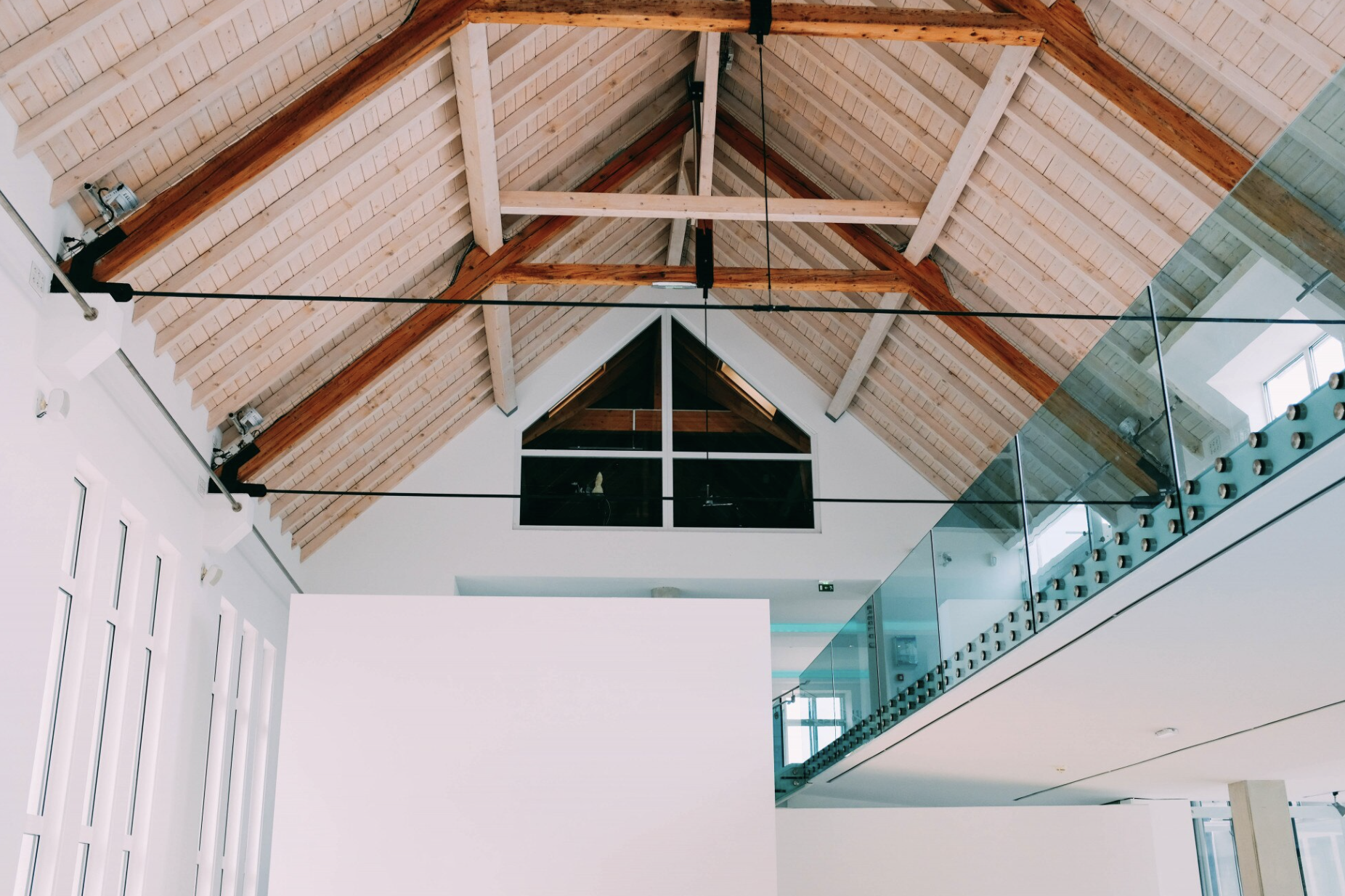 Intérieur moderne avec une grande mezzanine vitrée et un plafond cathédrale en bois clair, soutenu par des poutres apparentes.